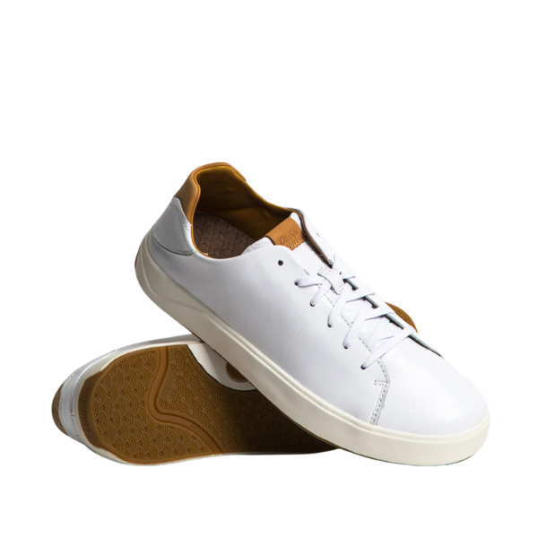 A pair of OLUKAI Mens Lae‘ahi Lī ‘Ili Leather Sneaker White with brown interiors and rubber soles, one upright and the other leaning against it, isolated on a white background.
