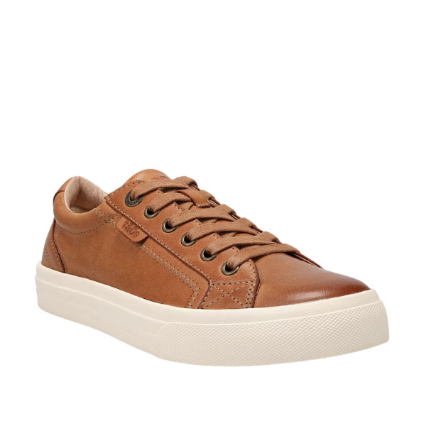 The Taos Womens Plim Soul Lux Caramel by TAOS is a brown leather sneaker with matching brown laces, metal eyelets, and a white rubber sole. It features a Curves & Pods footbed for comfort and is shown against a white background.