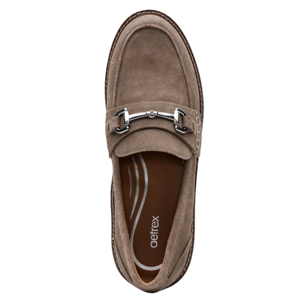 The AETREX Women's Collette Suede Taupe Loafer features a taupe suede upper, silver bit detail, visible stitching, and a cushioned insole with Aetrex branding for excellent arch support.