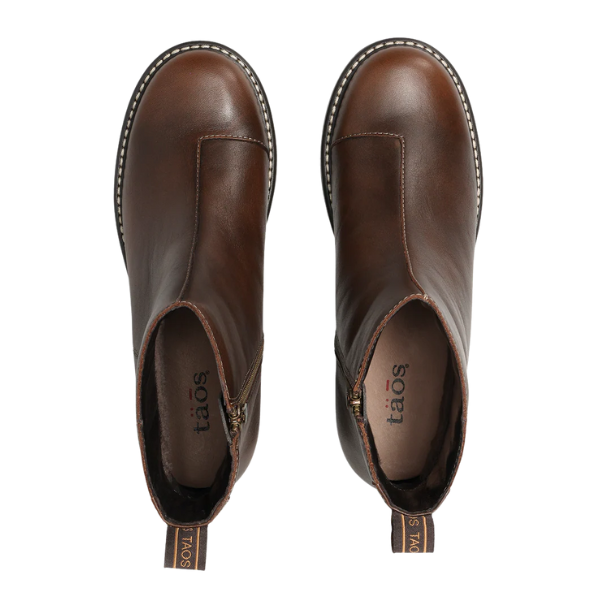 Top view of TAOS Taos Women's Uptown Dark Brown ankle boots with side zippers, visible sole stitching, pull tabs at the heels, and arch support, displayed on a white background.