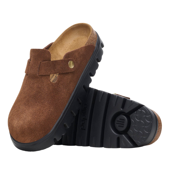 The BIRKENSTOCK Women's Boston Chunky Dark Tea clogs feature brown suede uppers, black rubber soles, a soft footbed, tread pattern, and gold-tone rivet detail, echoing the iconic Boston design. One clog stands upright; the other lies on its side.