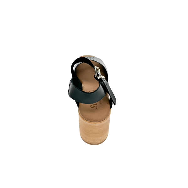 A Sovella Womens Lucia Black sandal by SOVELLA, featuring an ankle strap and wooden platform heel for foot pain relief, is shown from the back against a white background.