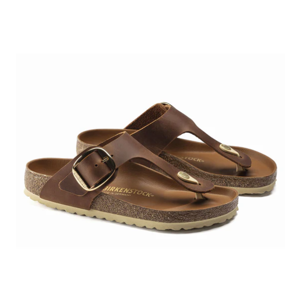 A pair of BIRKENSTOCK Womens Gizeh Big Buckle Oiled Leather Cognac sandals with adjustable big buckle straps, cork footbeds, and light-colored textured soles shown on a white background.