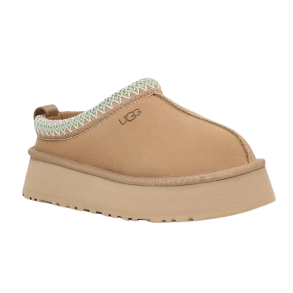 Meet the UGG Womens Tazz Slippers Sand: tan slip-on platform shoes featuring a thick outsole, decorative stitching, cozy UGGplush lining, and the signature UGG logo on the side.