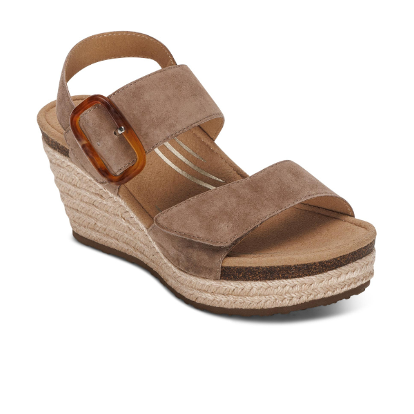 The Aetrex Women's Ashley Espadrille Wedge Taupe by AETREX WORLDWide INC features taupe suede, two wide straps with a large brown ankle buckle, a braided jute platform sole, and a cushioned memory foam footbed for comfort.