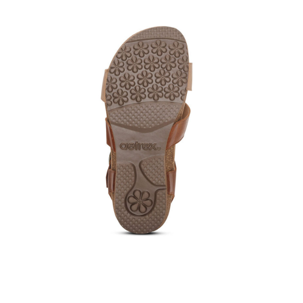 The sole of the Aetrex Womens Lilly Adjustable Quarter Strap Sandal in Walnut by AETREX WORLDWide INC is shown from below, displaying embossed flowers and the aetrex logo. Designed for comfort and arch support, with a white background.