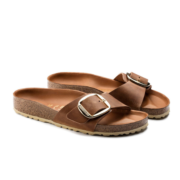 The BIRKENSTOCK Womens Madrid Big Buckle Cognac sandals feature Wide brown leather straps, oversized gold buckles, a supportive cork footbed, and textured rubber outsoles, displayed side by side on a white background.
