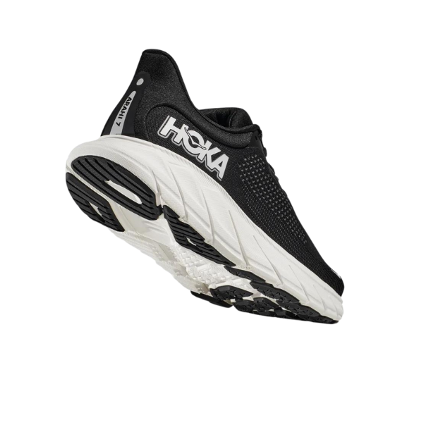 The HOKA Mens Arahi 7 Wide in Black/White is shown from a rear-side angle, featuring the J-Frame sole technology and HOKA branding. This stability running shoe is displayed isolated on a white background.