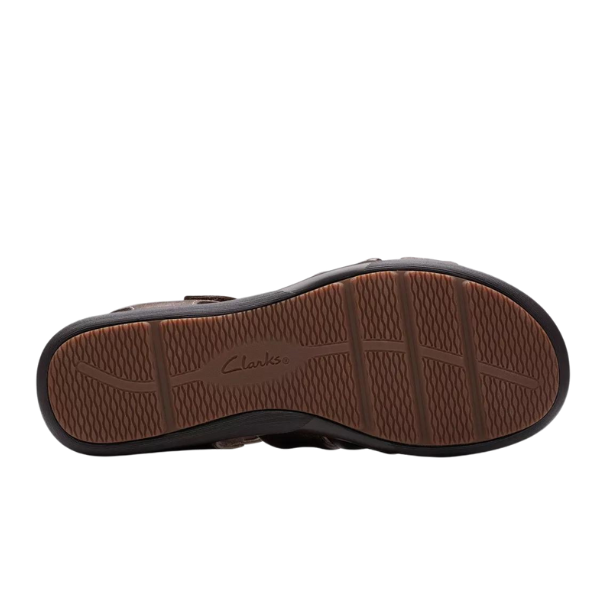 The image displays the sole of the CLARKS Womens Kitly Ave Bronze sandal, highlighting a textured, non-slip pattern with horizontal grooves and the CLARKS logo at the center.