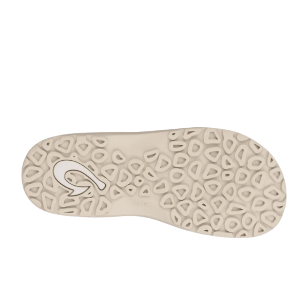 The image displays the sole of the OLUKAI Mens Ohana Graphite sandal, showcasing a beige base with a textured pattern of rounded, irregular geometric shapes and an abstract logo detail near the heel.