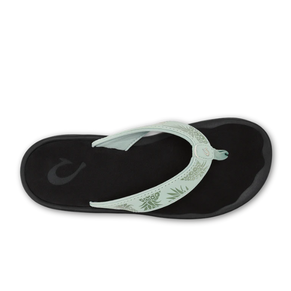 The OLUKAI Womens Ohana flip-flop in Mint/Swell Hua features a black sole, a light green floral strap, and is shown from above on a white background. This water-resistant sandal has a durable, non-marking rubber outsole.
