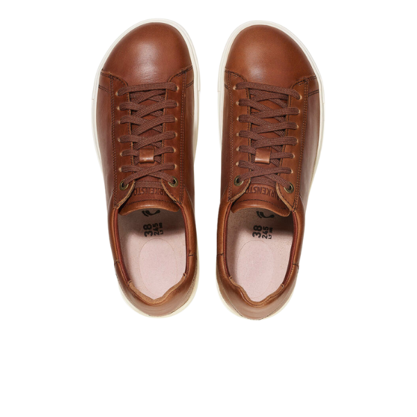 The BIRKENSTOCK Mens Bend Low Cognac sneakers feature brown natural leather uppers, white soles, matching laces with metal eyelets, a light beige inner lining, and a contoured footbed for comfort.
