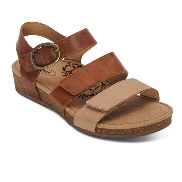 The Aetrex Womens Lilly Adjustable Quarter Strap Sandal in Walnut by AETREX WORLDWide INC features three brown straps with a gold buckle, a cork-textured sole, Memory Foam Footbed for comfort, and a floral-patterned heel for stylish support.