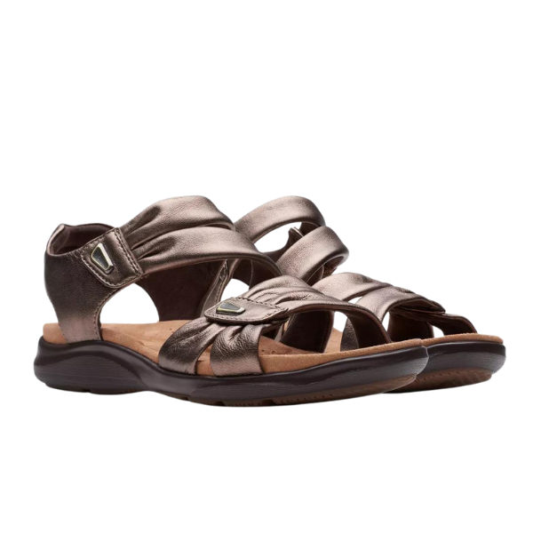 The Clarks Womens Kitly Ave Bronze sandals feature adjustable straps, a cushioned Contour Cushion footbed, low contoured rubber soles, decorative stitching, and a comfortable, casual design.
