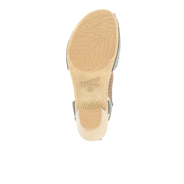 The image displays the bottom of a Dansko Womens Teagan Gunmetal sandal by DANSKO, featuring a textured tan sole with leaf-like patterns and the embossed dansko name and logo at the center.