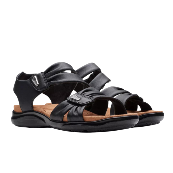The CLARKS Womens Wide Kitly Ave Black Leather sandals feature open toes, adjustable straps, and a Contour Cushion footbed for comfort and support, shown against a white background.