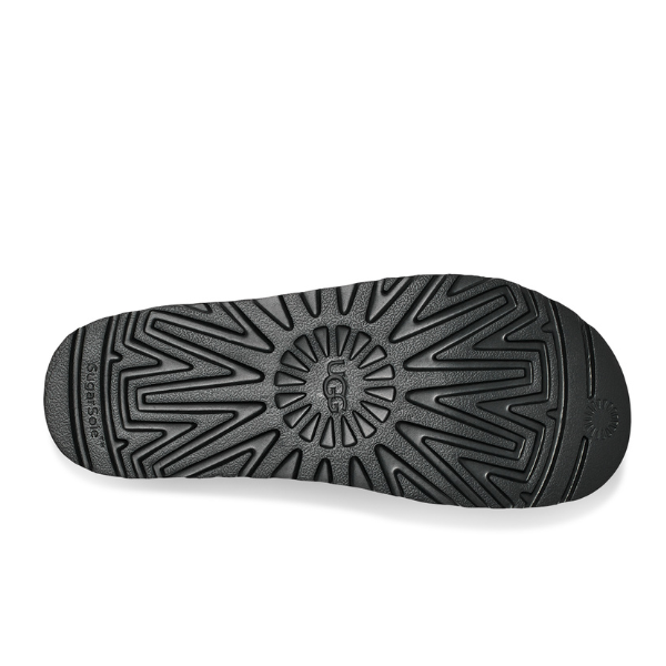 The UGG Womens Goldenstar Sandal Black features a black rubber SugarSole EVA sole with geometric tread and center UGG logo. Its angled lines offer grip and foot pain relief, with SugarSole labeled on the side.