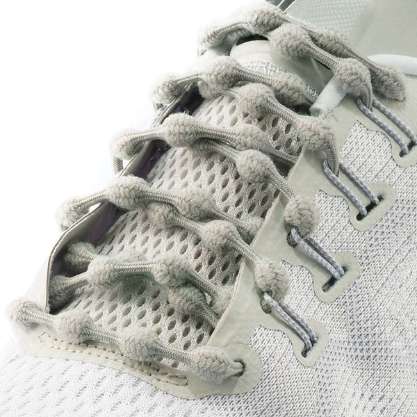 Close-up of a white athletic shoe with CATERPY RUN NO-TIE LACES GREY by CATERPY, featuring soft, thick, elastic laces with a knobby, wavy design threaded through fabric eyelets over a breathable mesh upper.