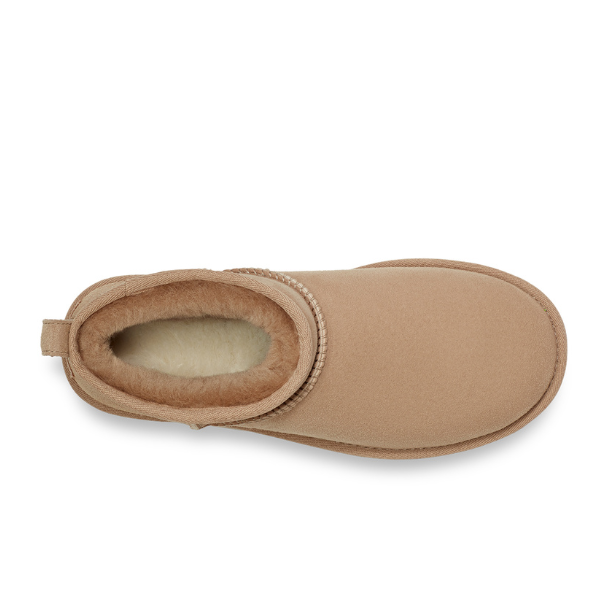 Top view of the UGG Womens Classic Ultra Mini Sand boot in tan, featuring a plush cream lining, visible stitching around the opening, and a pull tab at the back.