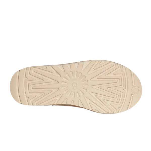 The image displays the beige rubber sole with a sunburst tread of the UGG Womens Tasman Slipper in Sand/Dark Cherry, featuring signature suede uppers for traction and style.