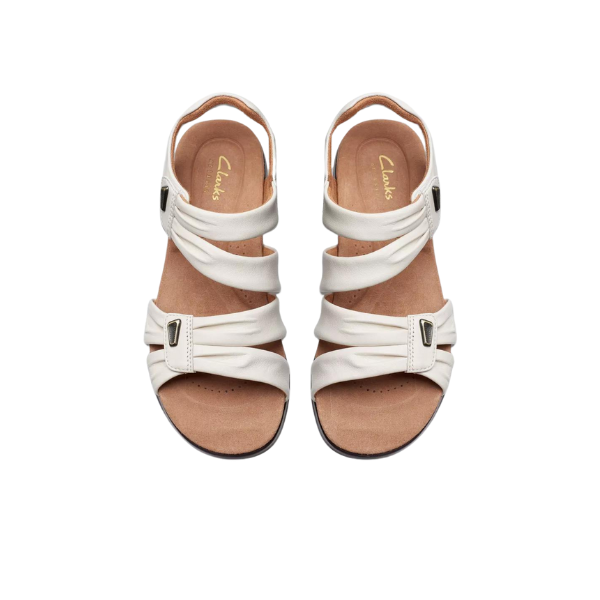 A pair of CLARKS Womens Wide Kitly Ave Sandals in white, featuring adjustable straps, tan insoles with Clarks branding, a black sole, and a contour cushion footbed for all-day comfort. Displayed side by side on a white background.