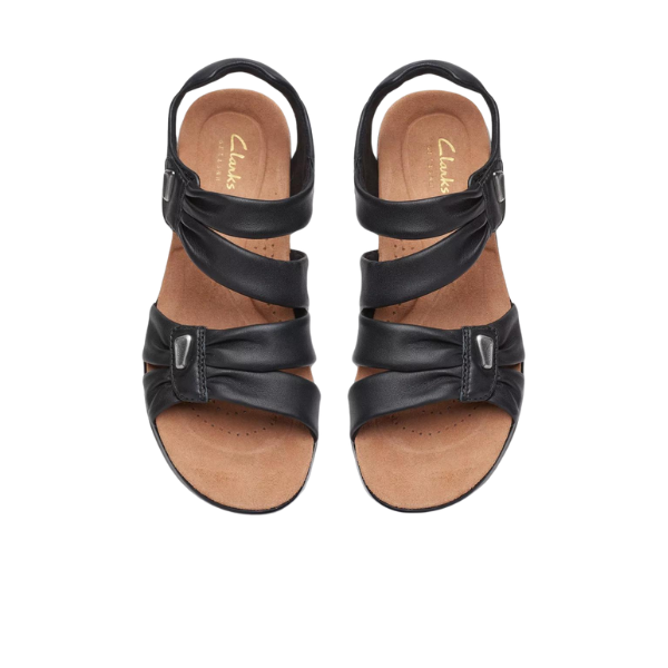 A pair of CLARKS Womens Wide Kitly Ave Black Leather sandals with three crisscross adjustable straps, open toes, and tan Contour Cushion footbed insoles, shown from above on a white background.