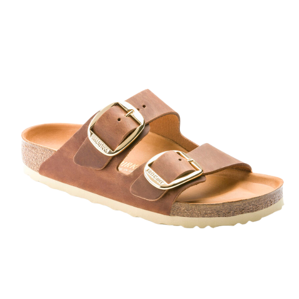 The BIRKENSTOCK Womens Arizona Big Buckle Cognac sandal features two Wide straps with large gold buckles, an oiled nubuck leather upper, a cork footbed, and a white textured sole.