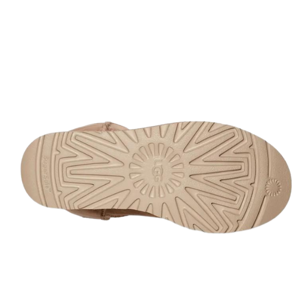 The bottom view of the UGG Womens Classic Short II Boots Sand by UGG shows a beige sandal with a patterned rubber sole, zigzag grooves, and circular designs for traction, offering comfort similar to that of the Classic Short II Boots.