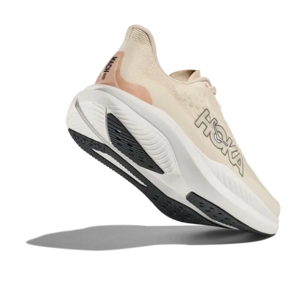 The HOKA Womens Mach 6 (Wide Width) in Vanilla is shown mid-air against a white background, angled to highlight the side logo and tread pattern—ideal for runners seeking supportive, Wide-width running shoes.