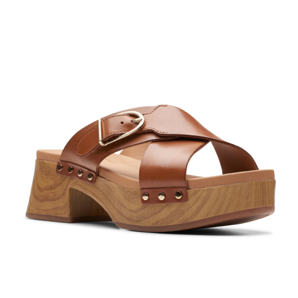 The Clarks Womens Sivanne Walk Tan sandal features tan crisscross leather straps, a gold buckle, metal studs, a chunky wooden platform sole, and CLARKS Cushion Soft comfort technology.