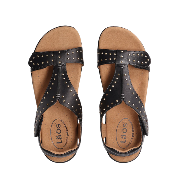 The Taos Womens Show Stopper Black sandals by TAOS feature tan footbeds, decorative metal studs on the straps, and Soft Support™ for exceptional foot pain relief.