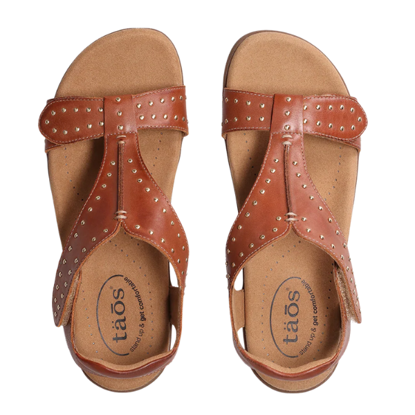 A pair of TAOS Womens Show Stopper Cognac sandals in brown leather with metallic studs, open toes, and adjustable straps, shown from above. Features Soft Support insoles with Cool Recovery Foam and TAOS branding near the heel.