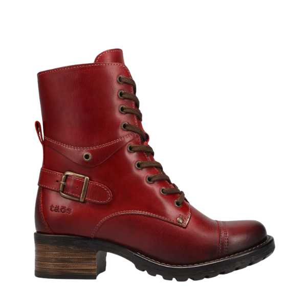 The Taos Women’s Crave Boot Red is a red leather ankle boot by TAOS with a low stacked heel, side buckle, black eyelets, brown laces, taös branding near the heel, and built-in arch support for comfort.
