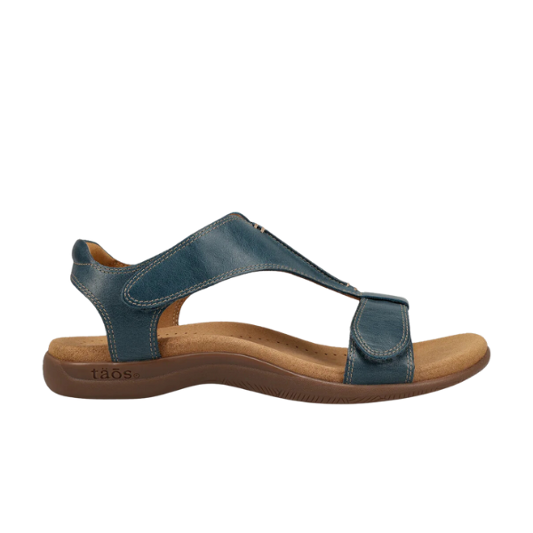 The TAOS Taos Womens The Show Petrol Blue sandal features blue leather, adjustable Velcro straps, an open toe, a tan antimicrobial cushioned footbed, and a brown rubber sole. Shown in side view.