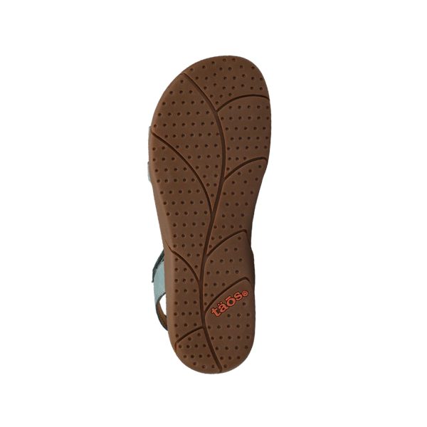 The image displays the sole of a TAOS Womens Trophy 2 sandal in teal, featuring a textured, leaf-patterned bottom and “taös” printed in orange near the heel. The white background accentuates its supportive design for foot comfort.