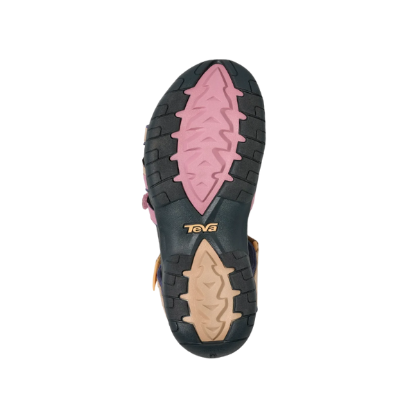 The image shows the sole of the Teva Womens Tirra Root Light Multi sandal, with a pink and tan zigzag tread pattern, black rubber edges for grip, arch support design, and the yellow Teva logo near the heel.