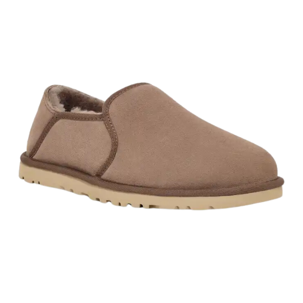 The UGG Mens Kenton Caribou is a tan slip-on suede slipper with plush sheepskin lining, a light rubber sole, and a convenient collapsible heel for versatile wear.