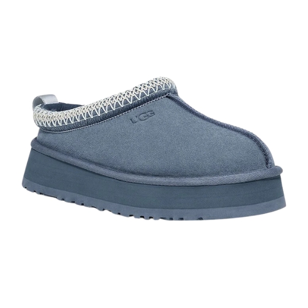 The UGG Womens Tazz Slippers in Desert Blue feature a thick platform sole, rounded toe, soft upper, decorative ankle stitching, embossed UGG logo, and cushioned design for stylish comfort and foot pain relief.