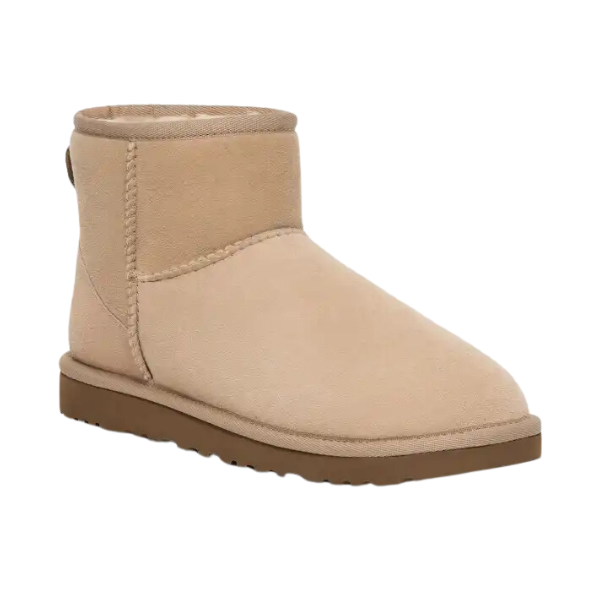 The UGG Womens Classic Mini II Boot Sand is a tan suede ankle boot with visible stitching, rounded toe, and flat brown rubber sole. Soft lining provides comfort and foot pain relief. Inspired by classic sheepskin boots from UGG.