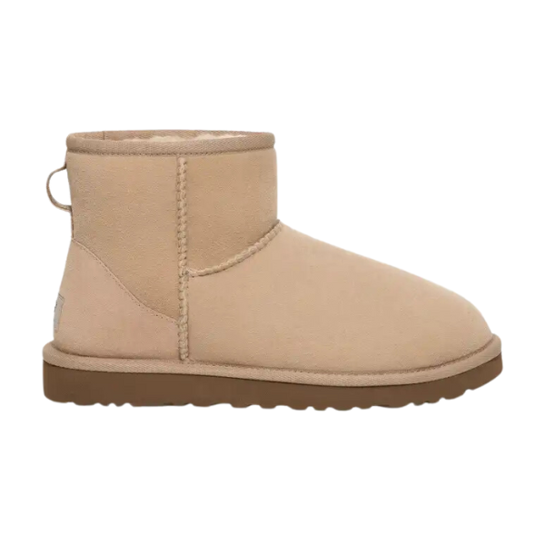 The UGG Womens Classic Mini II Boot Sand features a tan suede exterior, rounded toe, visible stitching, flat brown rubber sole, and a soft light-colored lining for added comfort—classic style and iconic UGG comfort.