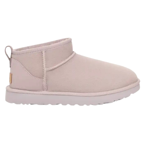 The UGG Womens Classic Ultra Mini Boot Pale Smoke is a light beige suede ankle-high boot with a pull tab, textured rubber sole, and sheepskin lining for comfort, shown from the side.