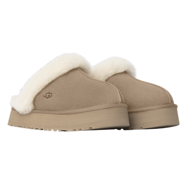 The UGG Womens Disquette Sand slippers feature signature sheepskin and suede, a thick light-colored shearling trim, and a textured rubber sole, displayed from the side on a white background.