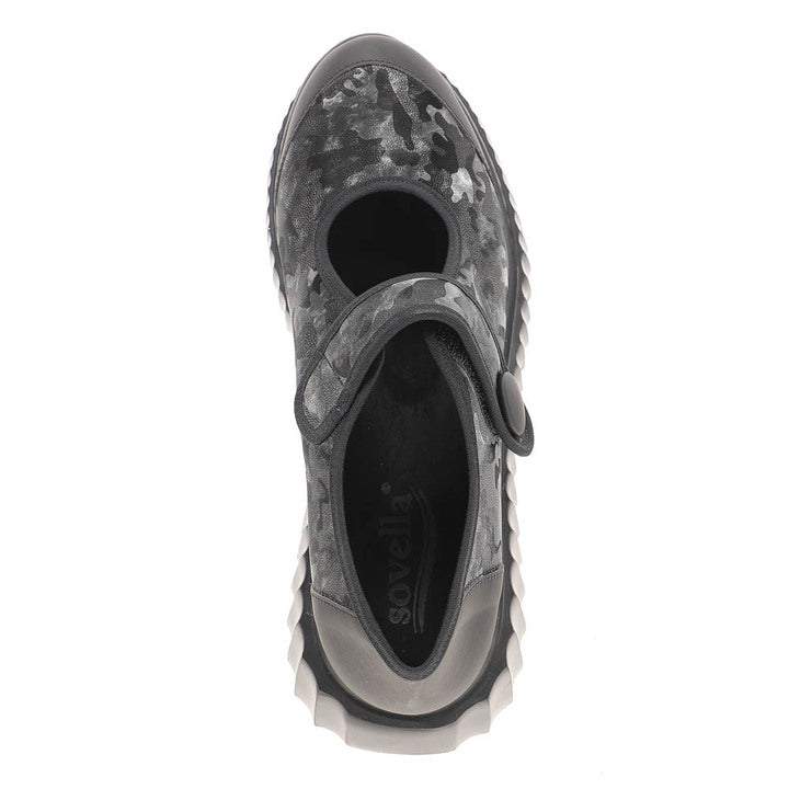 The SOVELLA Sovella Womens Jessica Black Camo features a sporty top view, black and grey camo pattern, thick ridged sole, and one strap with a round button closure across the instep.