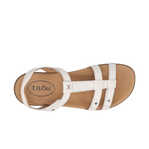 Top view of the Taos Womens Trophy 2 Icee sandal by TAOS, featuring white leather straps, a tan cushioned footbed with logo on the heel, metallic rivet accents, and arch plus metatarsal support for all-day comfort.