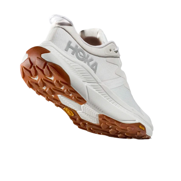 The HOKA Womens Transport White shoe features a thick, textured brown sole and detailed tread, with the HOKA brand visible—perfect for those seeking stylish, sustainable footwear.