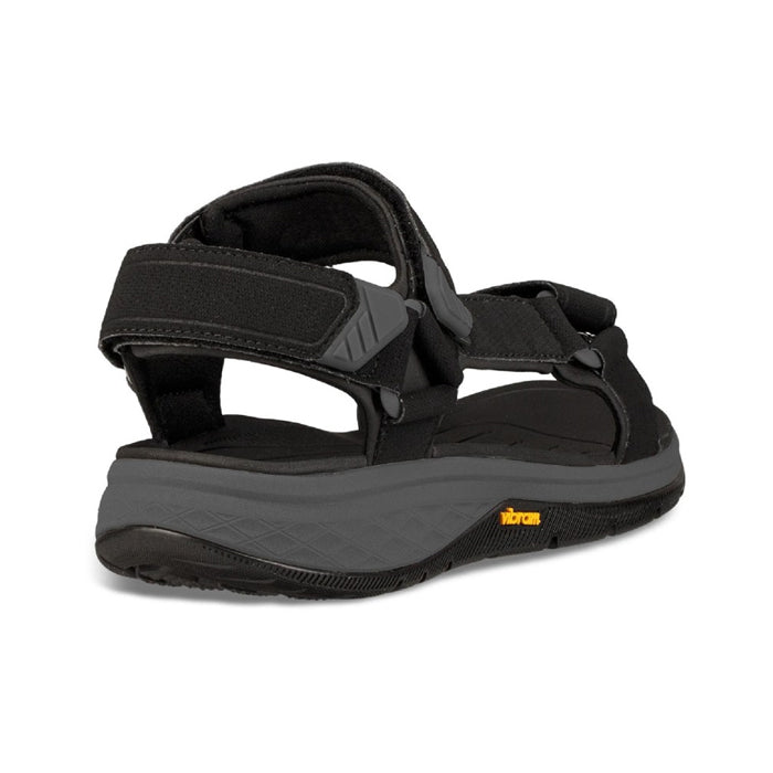 The Teva Mens Strata Universal Black sandal, shown from the back, features adjustable Velcro straps and a textured sole with the yellow Vibram logo—designed by Teva for comfort and foot pain relief on long walks.