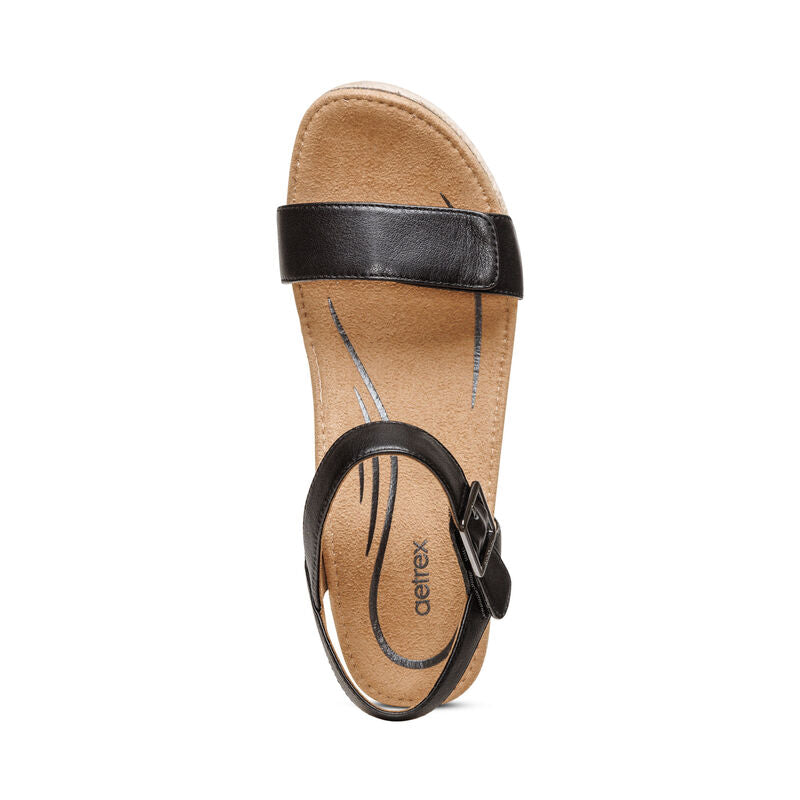 A black leather Aetrex Womens Sydney sandal with a buckle ankle strap and tan cushioned memory foam footbed, viewed from above. The insole features the Aetrex brand name and offers signature arch support for comfort.