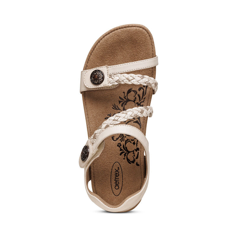 The Aetrex Womens Jillian Ivory sandal features braided straps, a floral-print insole, round metal buckles, and plush memory foam cushioning for comfort. Shown in ivory against a white background.