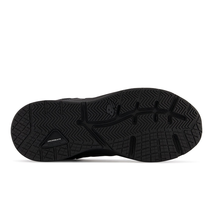 The image displays the black rubber outsole of the NEW BALANCE Womens WX857 V3 Wide Black, highlighting textured zigzag and grid patterns for traction, ROLLBAR technology, and a small embossed logo near the center.