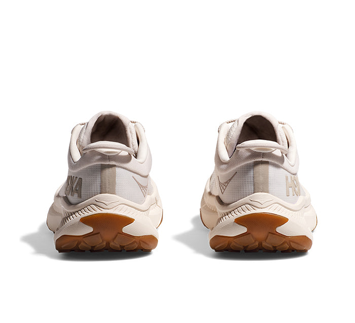 Rear view of a pair of HOKA Womens Transport Eggnog sneakers, featuring sustainable materials and light brown soles, side by side on a white background. The HOKA logo appears on the heels—an everyday comfort shoe.